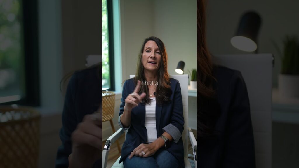 Woman in a navy blazer sitting in an office chair, speaking and gesturing with her hand